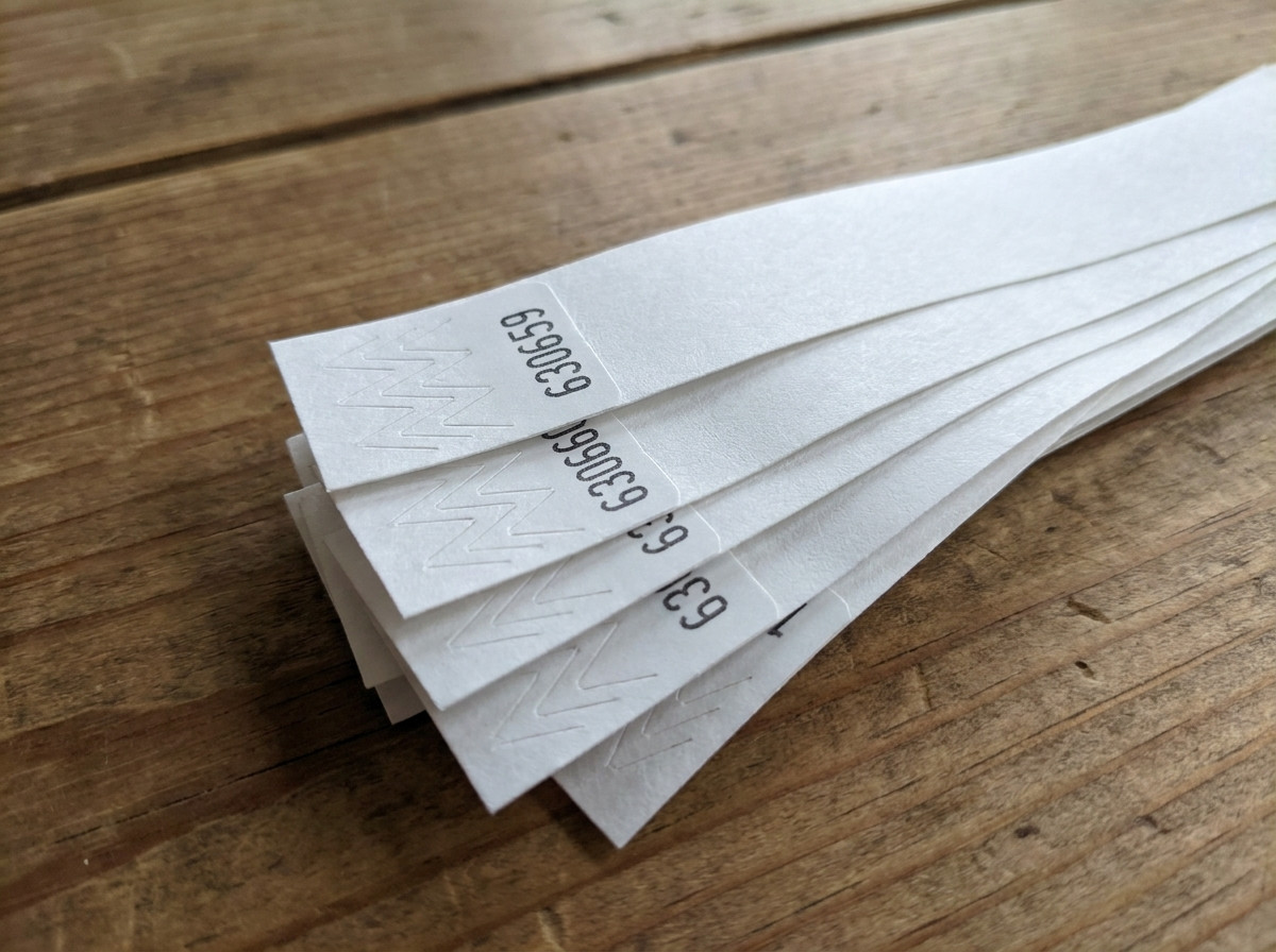 Gros plan sur des bracelets Tyvek avec numérotation séquentielle imprimée en noir, disposés en éventail sur une table de contrôle d'accès lors d'un événement